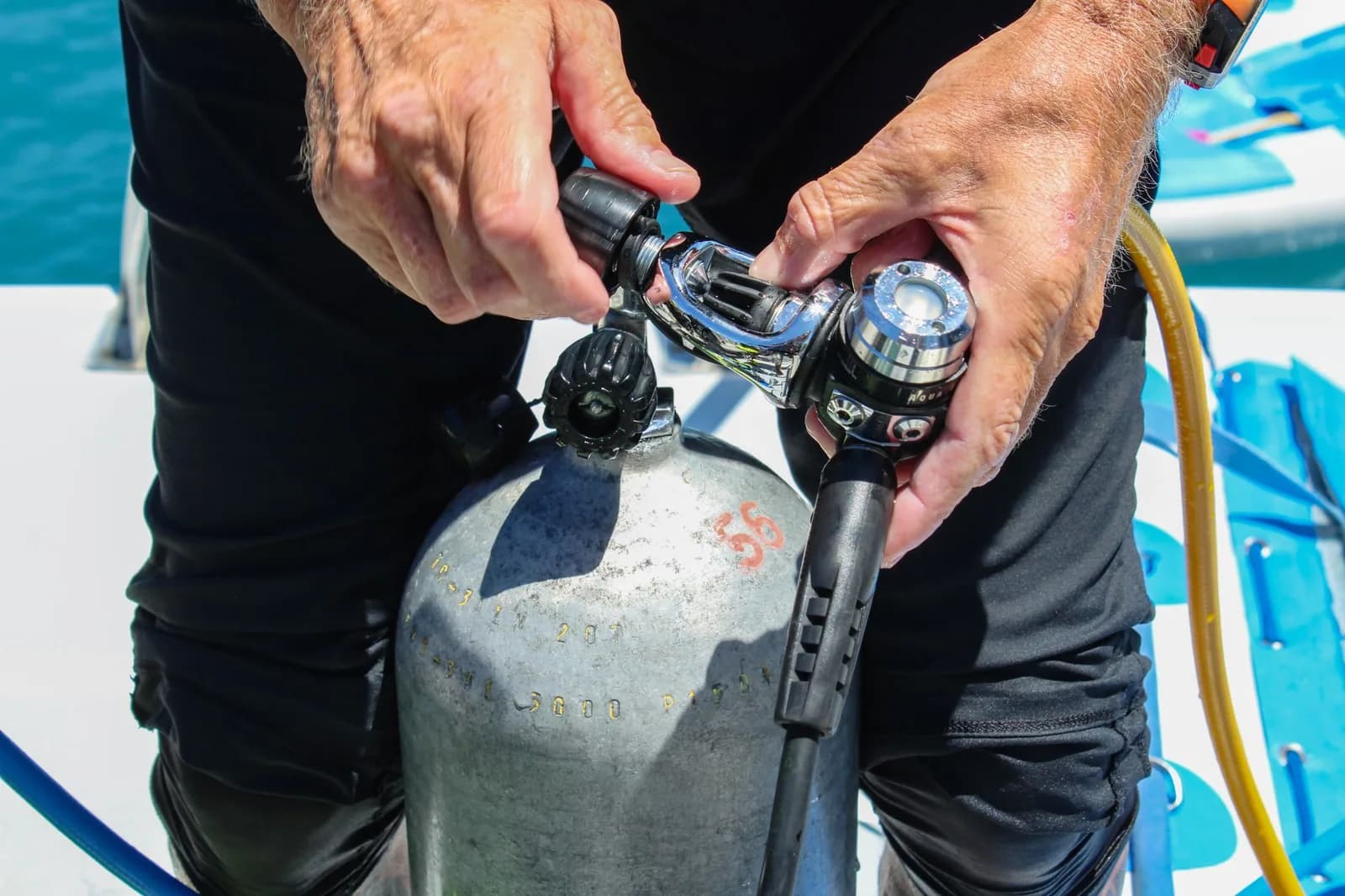 Gros plan sur des mains raccordant un détendeur sur une bouteille de plongée à bord d'un bateau avant la mise à l'eau