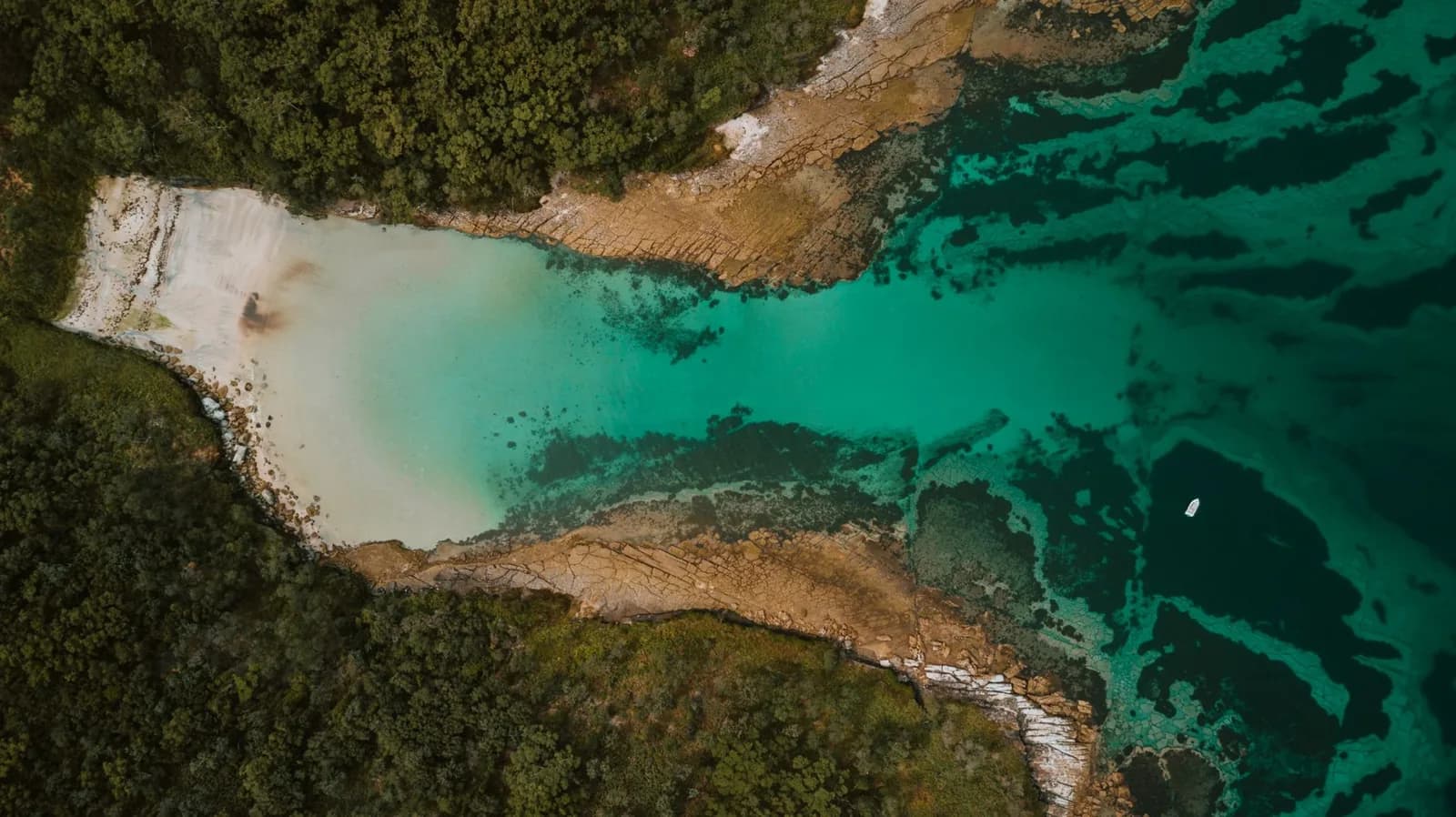 Vue aérienne d'une baie aux eaux turquoise bordée de forêt dense et de roches ocre, paysage côtier évoquant le Grand Sud de la Nouvelle-Calédonie