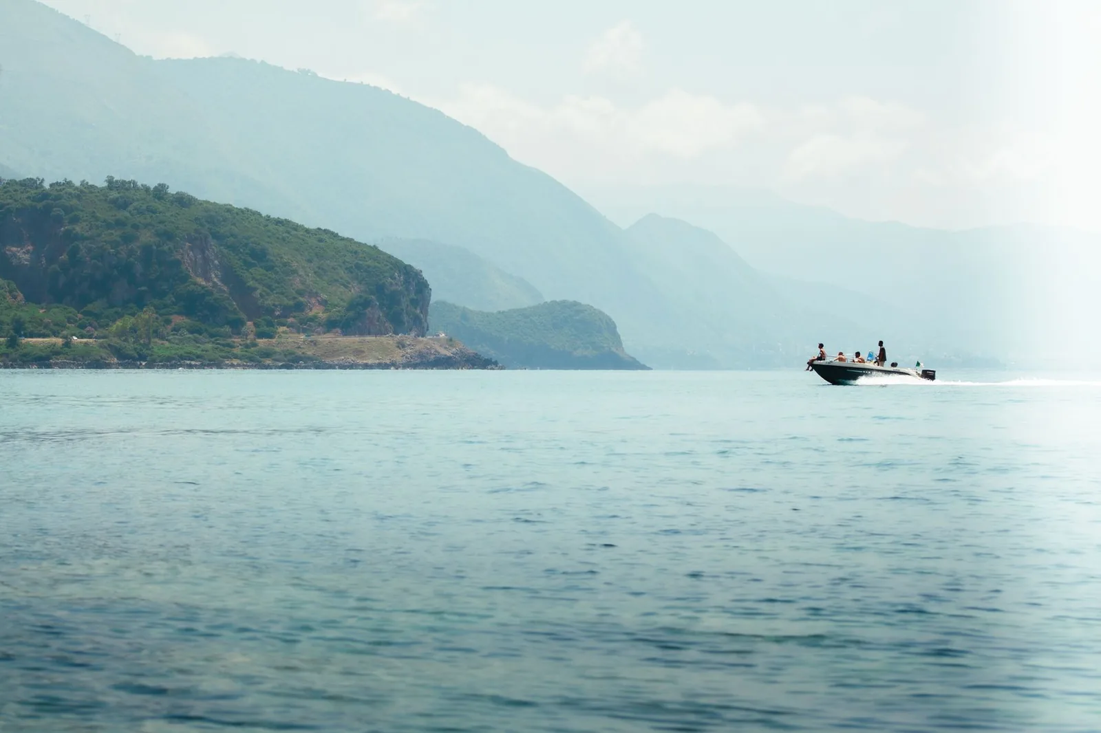 Bateau à moteur avec plusieurs passagers naviguant en mer le long d'une côte verdoyante et montagneuse