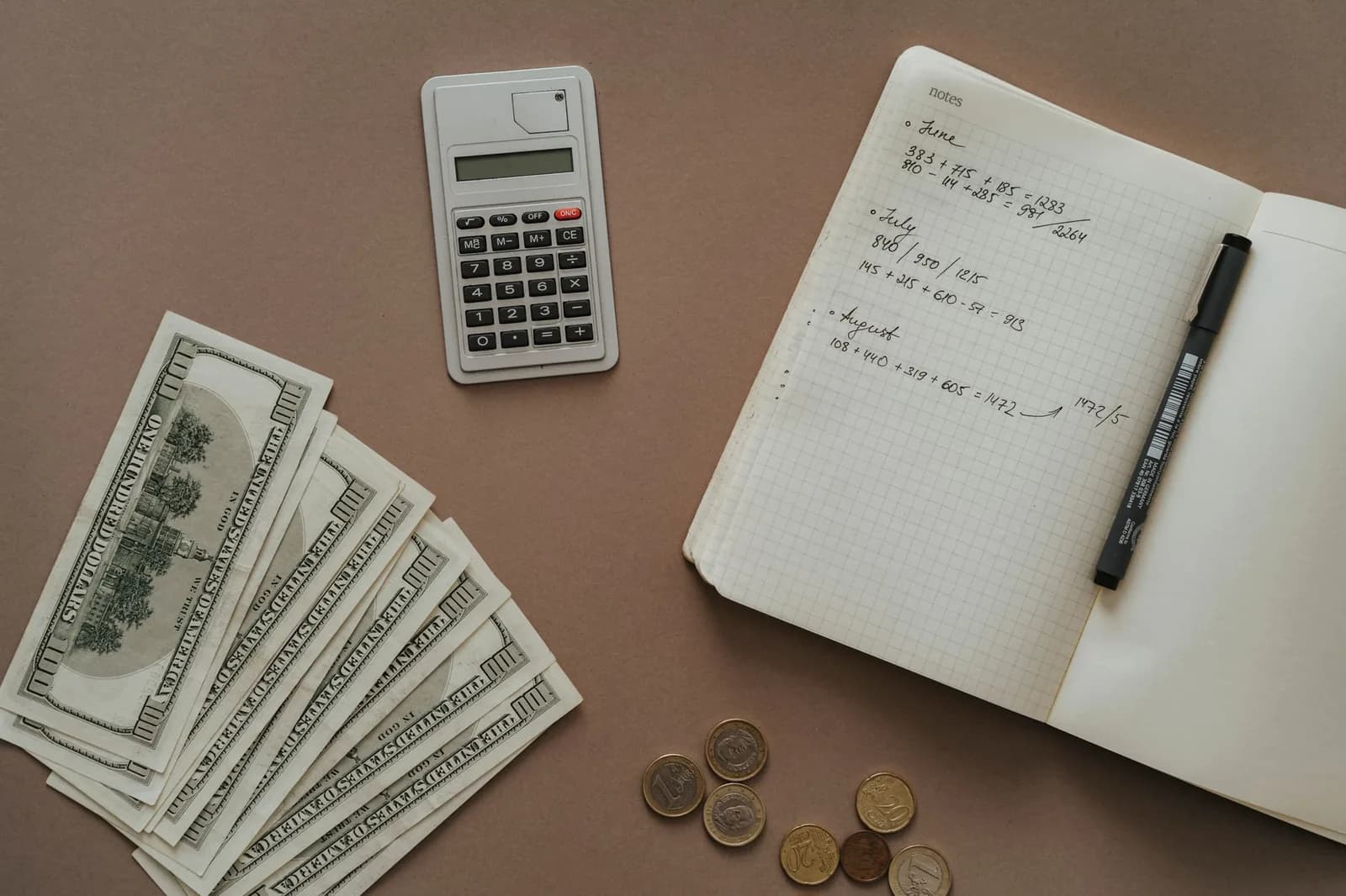 Calculatrice, billets, pièces et carnet de calculs budgétaires mensuels sur un bureau, pour estimer les frais d'installation et l'épargne à prévoir avant de partir à Nouméa