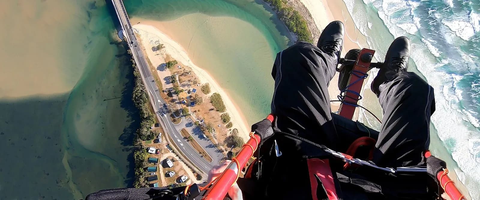 Survol d'un lagon en paramoteur (ULM) : vue plongeante sur la plage et les eaux turquoise depuis le harnais du pilote, l'un des modes d'observation aérienne