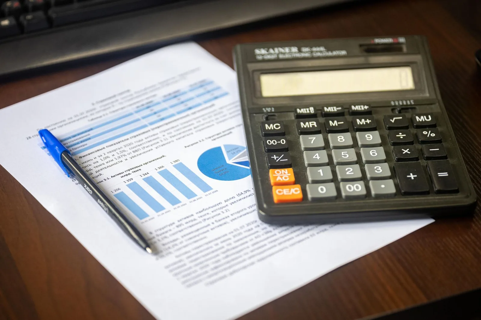 Calculatrice posée sur un rapport financier avec graphiques, évoquant la simulation chiffrée d'une réduction d'impôt