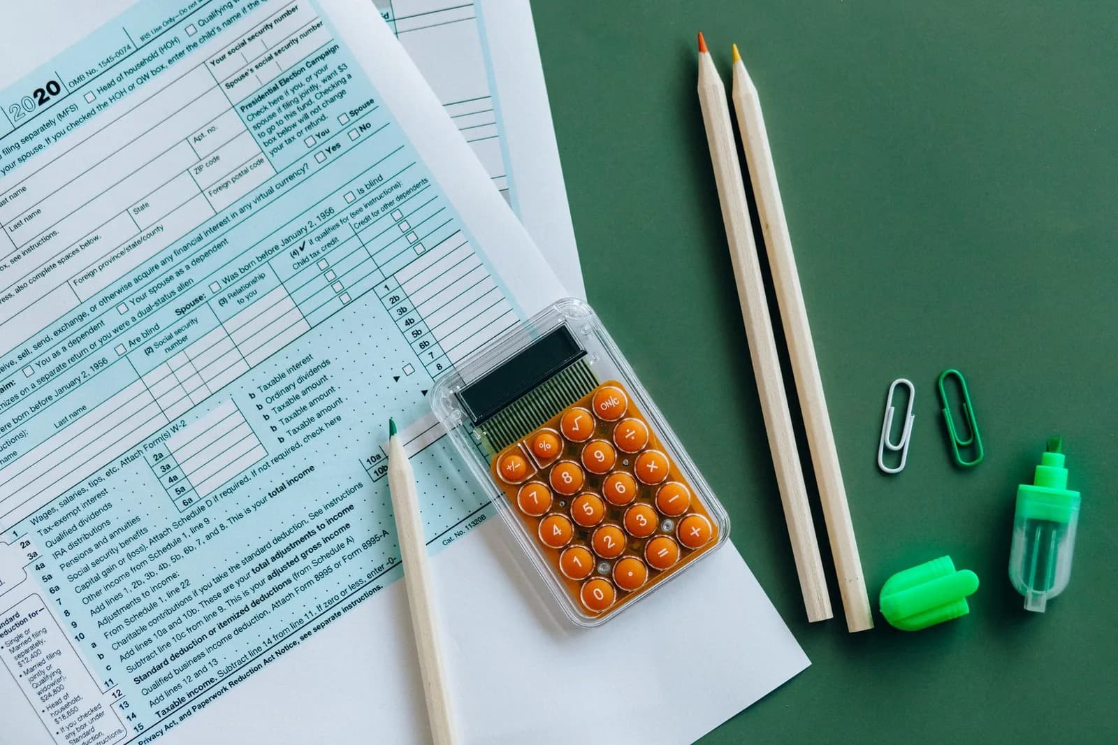 Formulaire fiscal, calculatrice orange et crayons posés sur un bureau, illustrant la déclaration de revenus