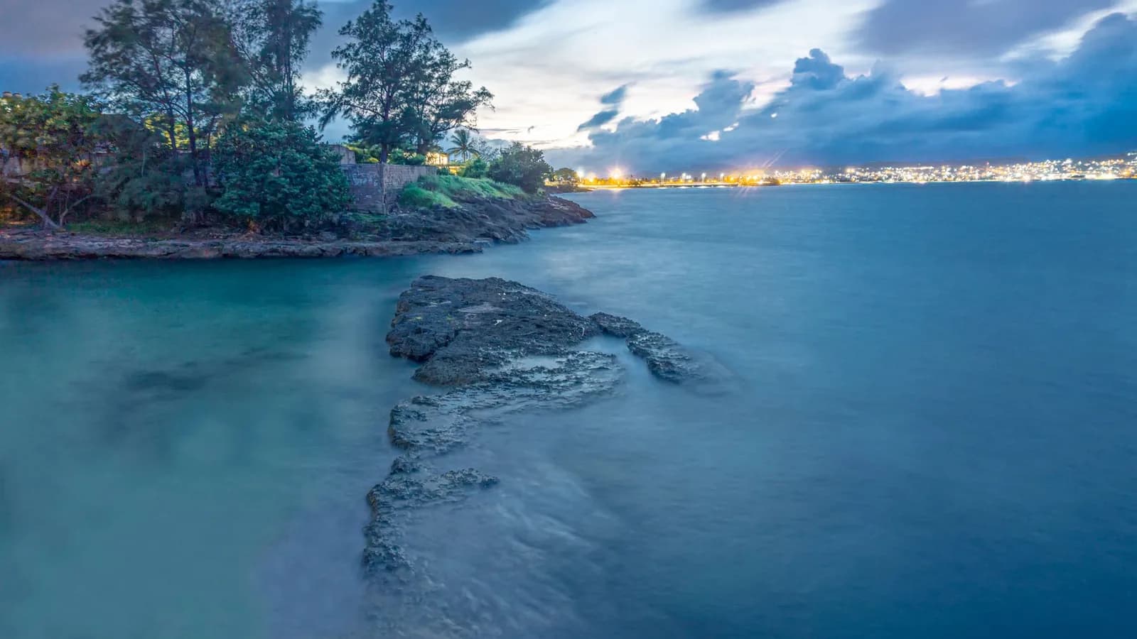 Littoral urbain au crépuscule avec les lumières d'une ville en bord de baie, évoquant Nouméa en Nouvelle-Calédonie