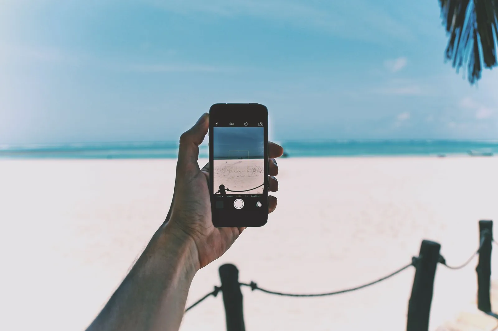 Smartphone tenu à bout de bras devant une plage de sable blanc, réseau mobile en Nouvelle-Calédonie