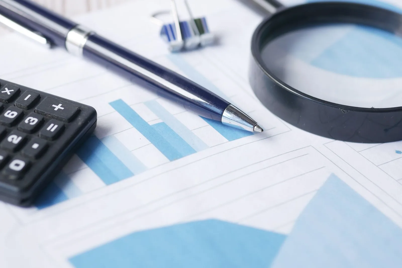 Mains manipulant des documents et une calculatrice sur un bureau, devant un ordinateur (image générique d'illustration)