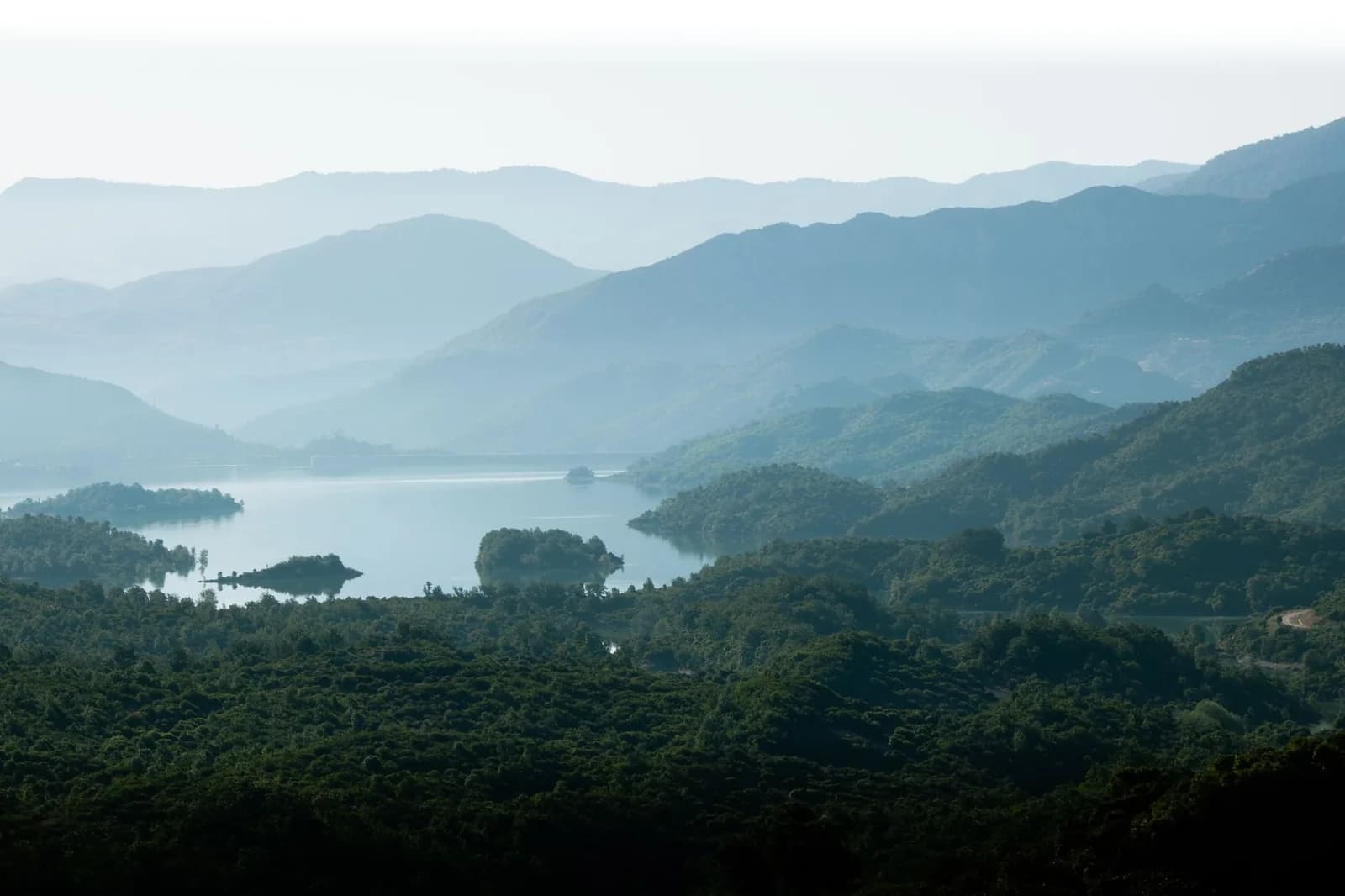Lac cerné de collines boisées dans une lumière matinale brumeuse, paysage évoquant le lac de Yaté et les Grands Lacs du Grand Sud calédonien