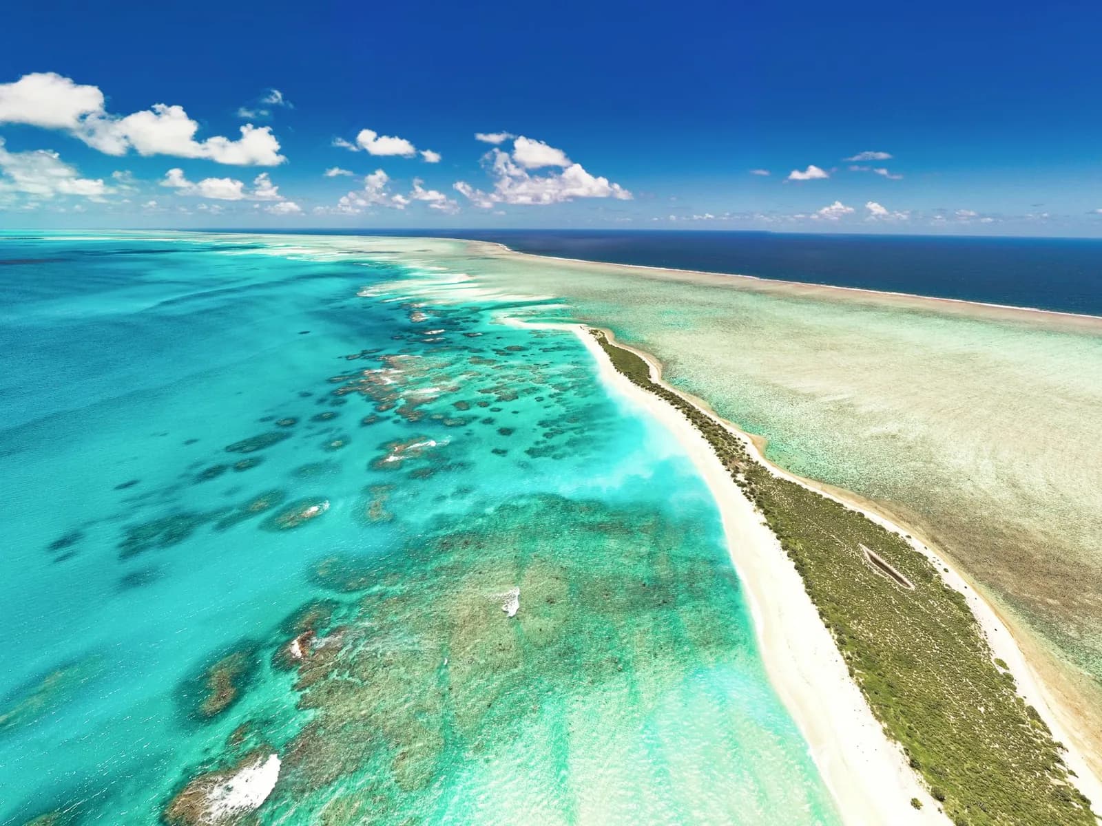 Vue aérienne d'un îlot de sable blanc cerné d'un lagon aux eaux turquoise