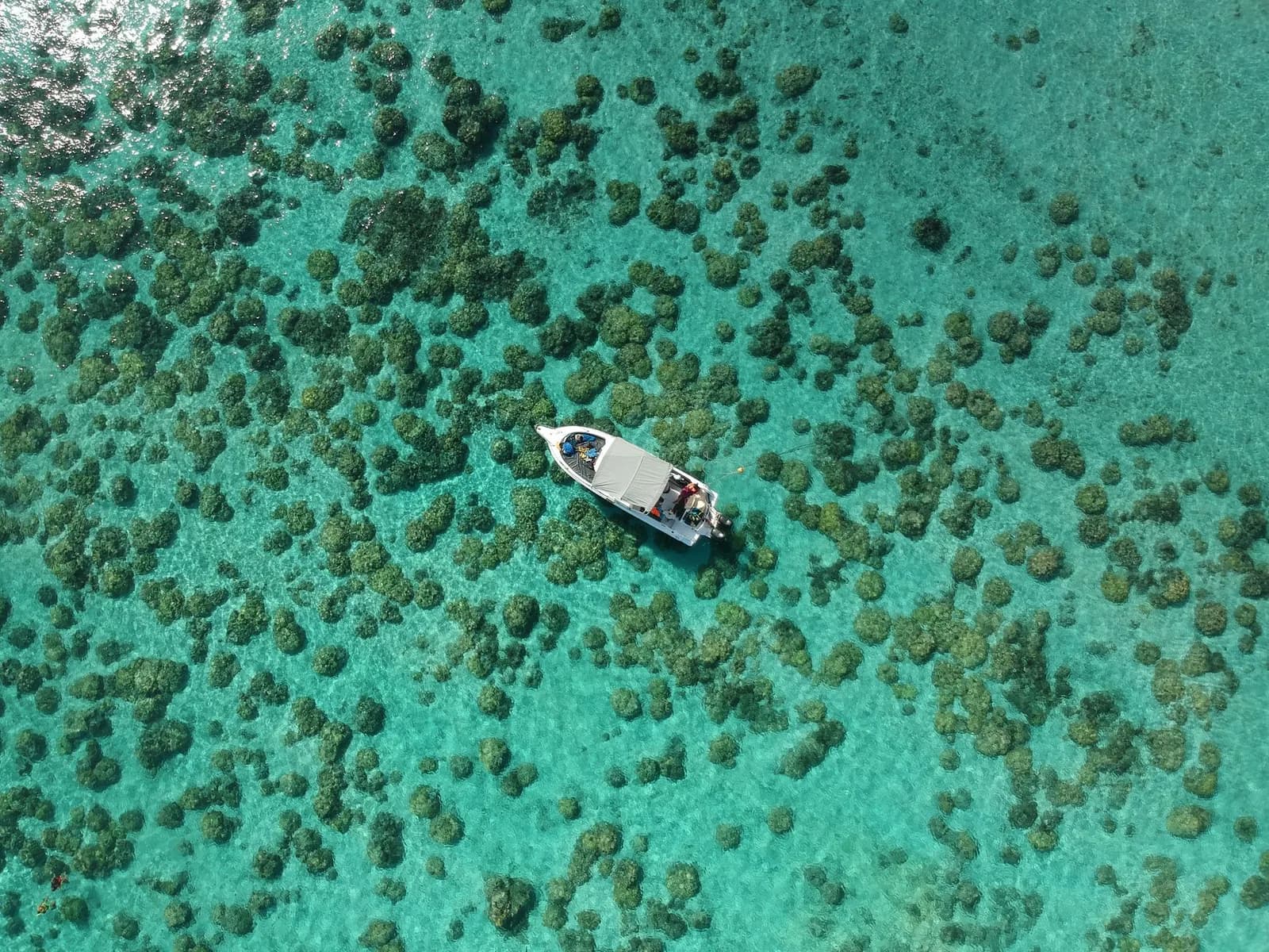 Vue aérienne d'un lagon turquoise parsemé de patates de corail, un petit bateau à l'ancre, décor propice au snorkeling
