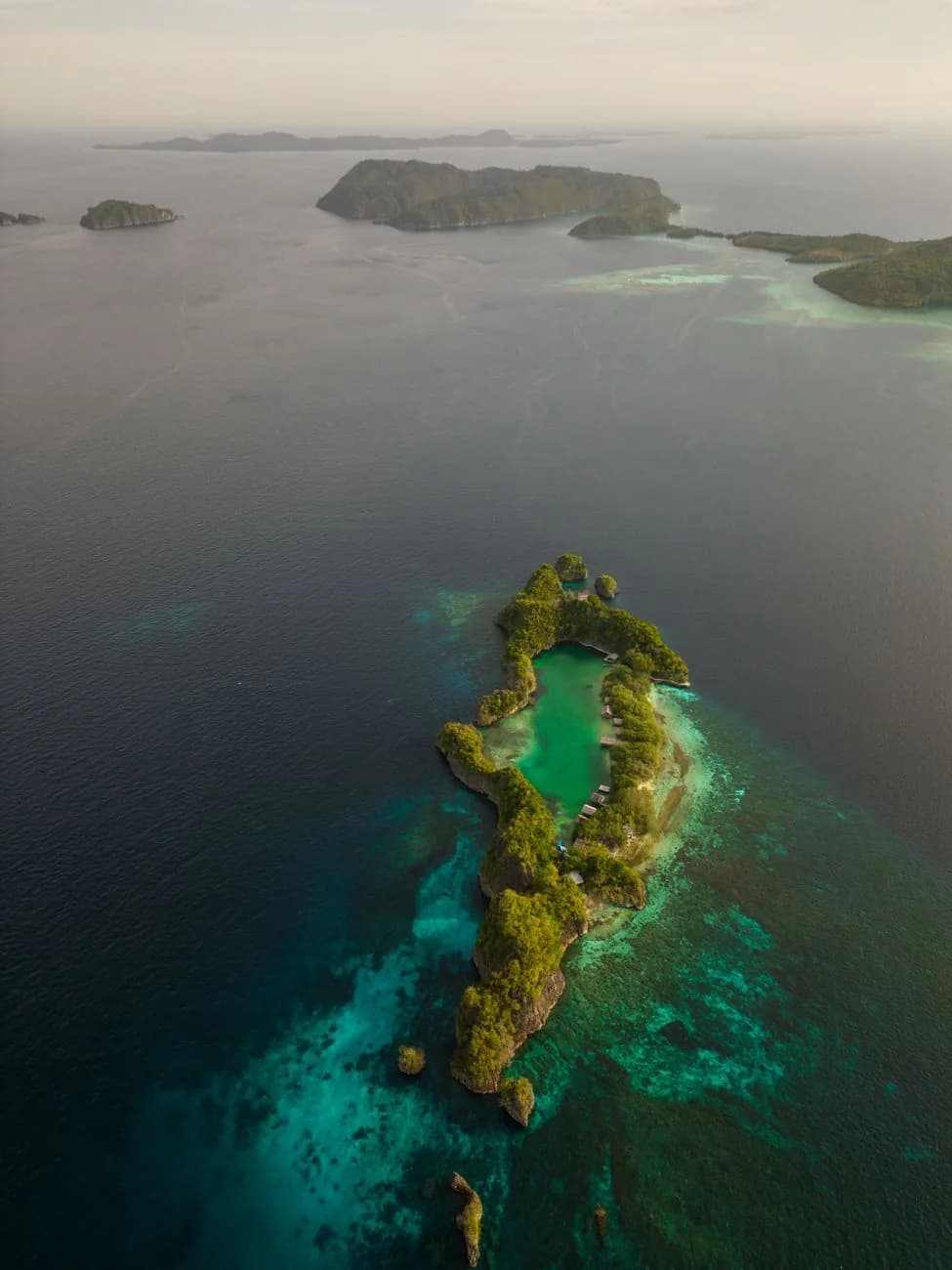 Vue aérienne d'un îlot tropical verdoyant entouré d'un lagon aux nuances de bleu, au large de Nouméa