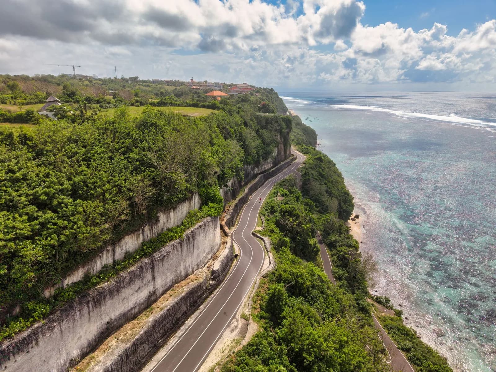 Route bitumée sinueuse longeant un littoral tropical au-dessus d'un lagon turquoise