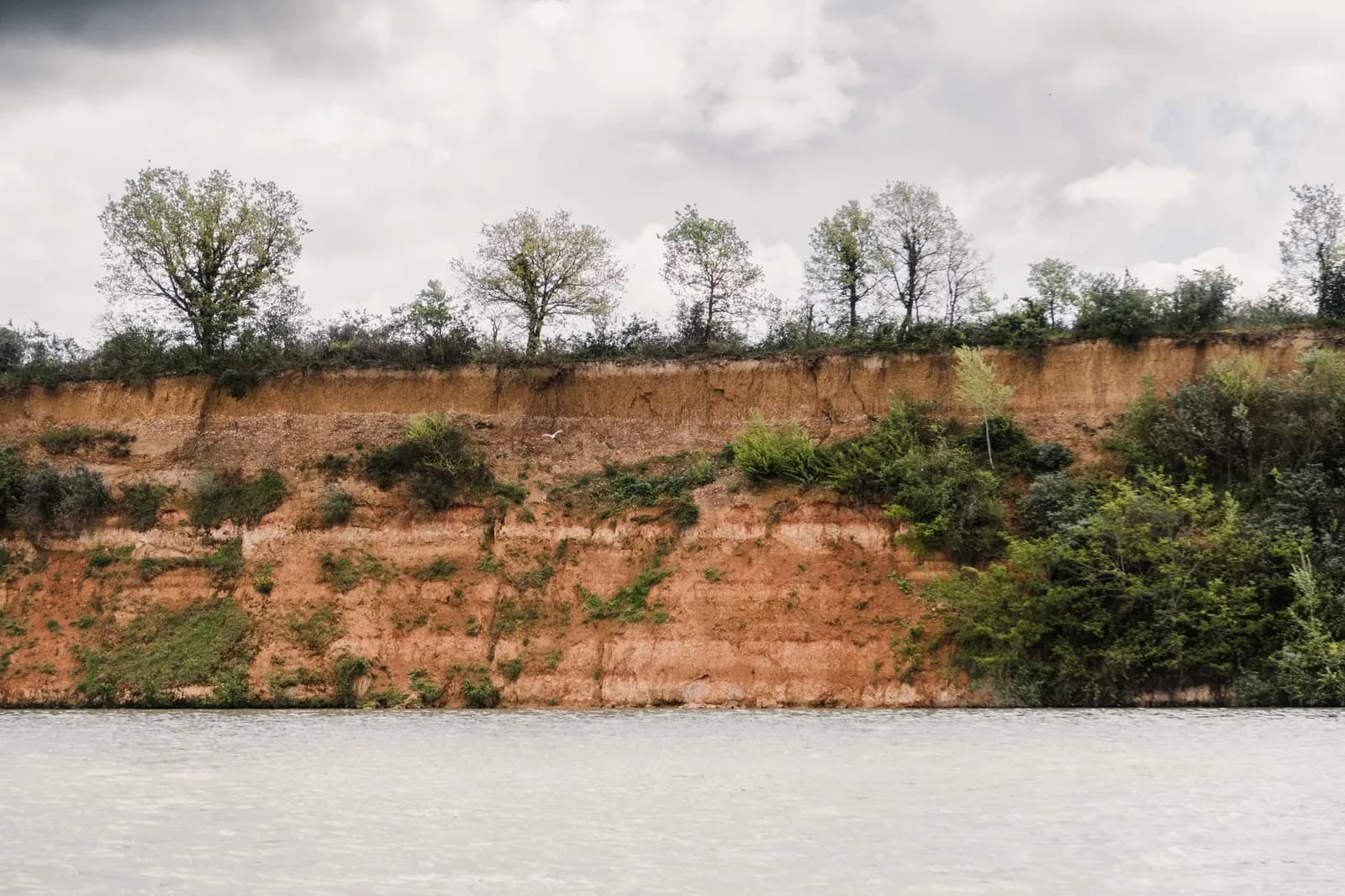 Berge de terre rouge latéritique bordée de végétation au bord d'un plan d'eau, évoquant les paysages de terre rouge du sud