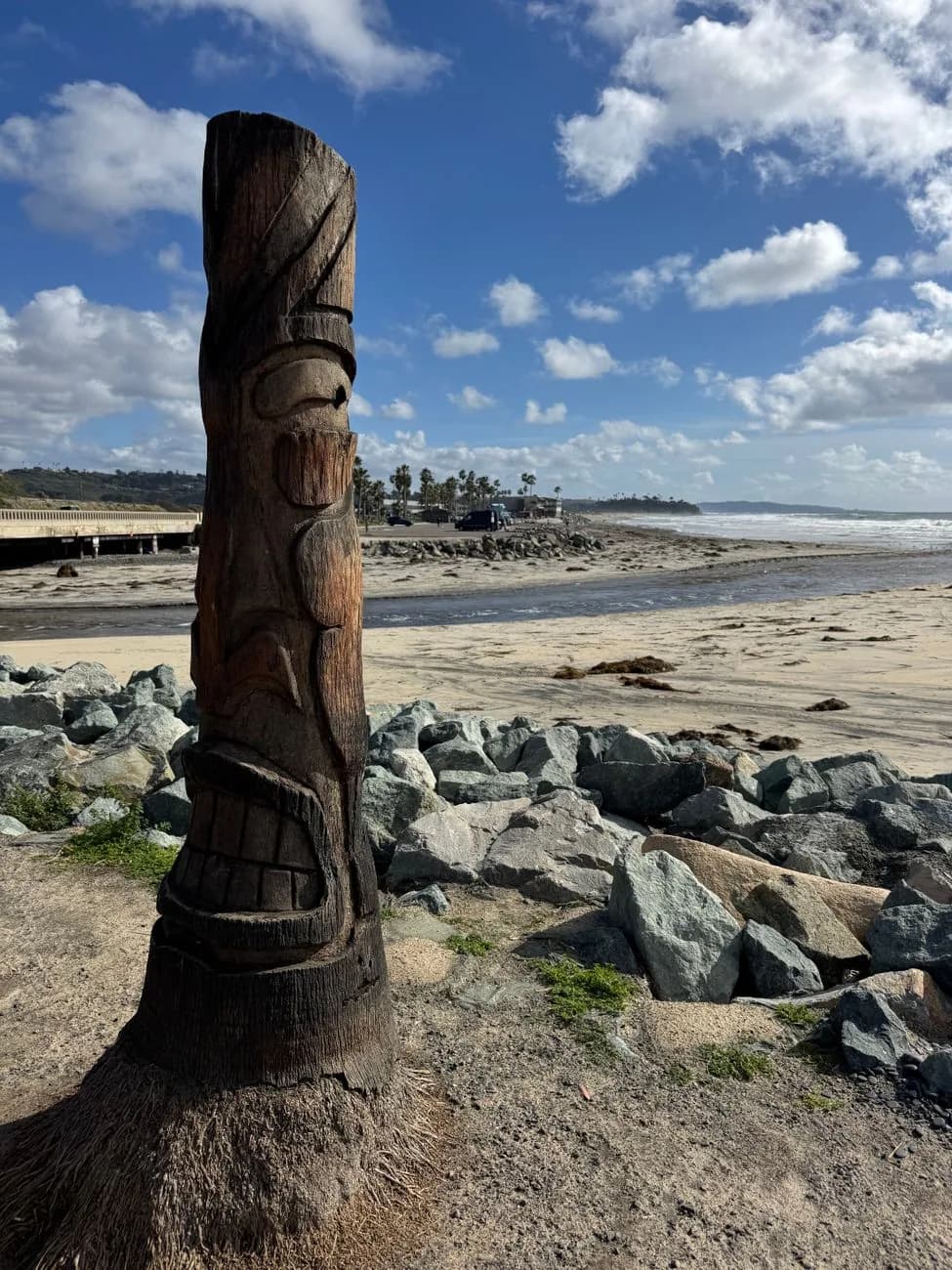 Totem en bois sculpté dressé au bord d'une plage face à l'océan Pacifique